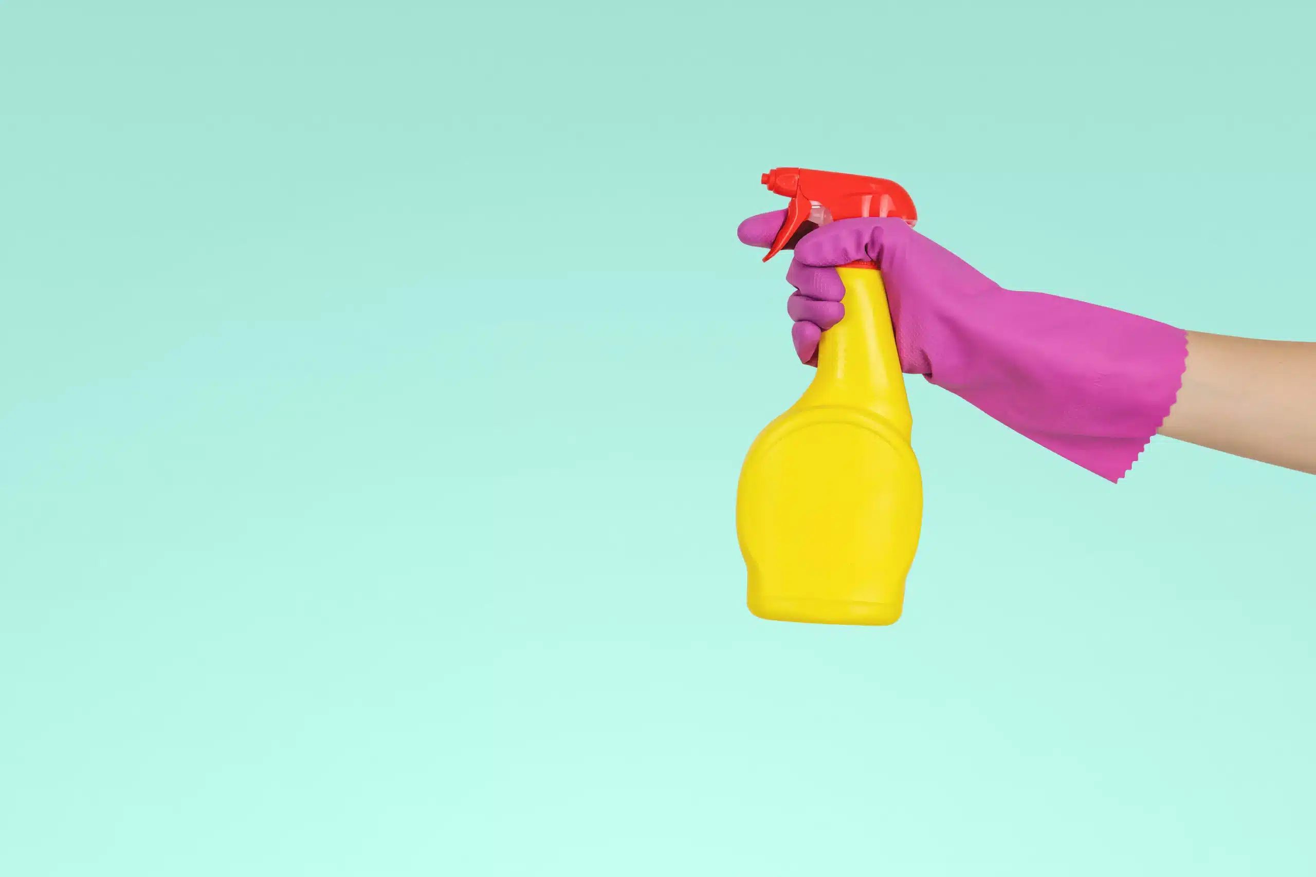Eine Hand, die eine Putzflasche mit einem Handschuh hält als Zeichen für den Frühjahrsputz