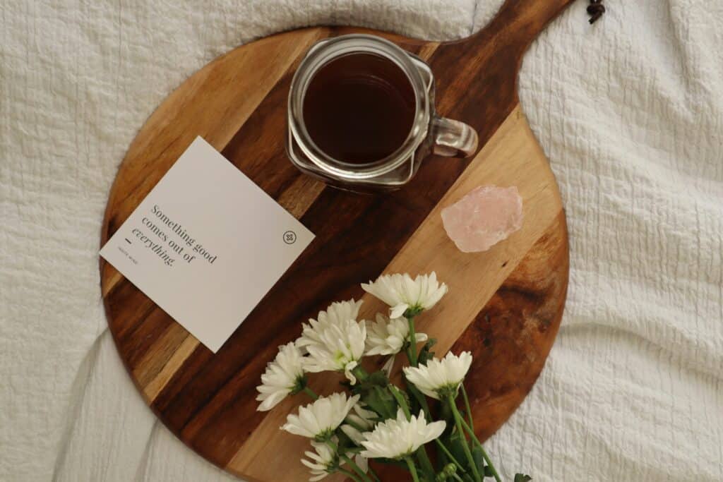 Ein Holzbrett mit einer Affirmation, Kaffee und Blumen auf einem Bett