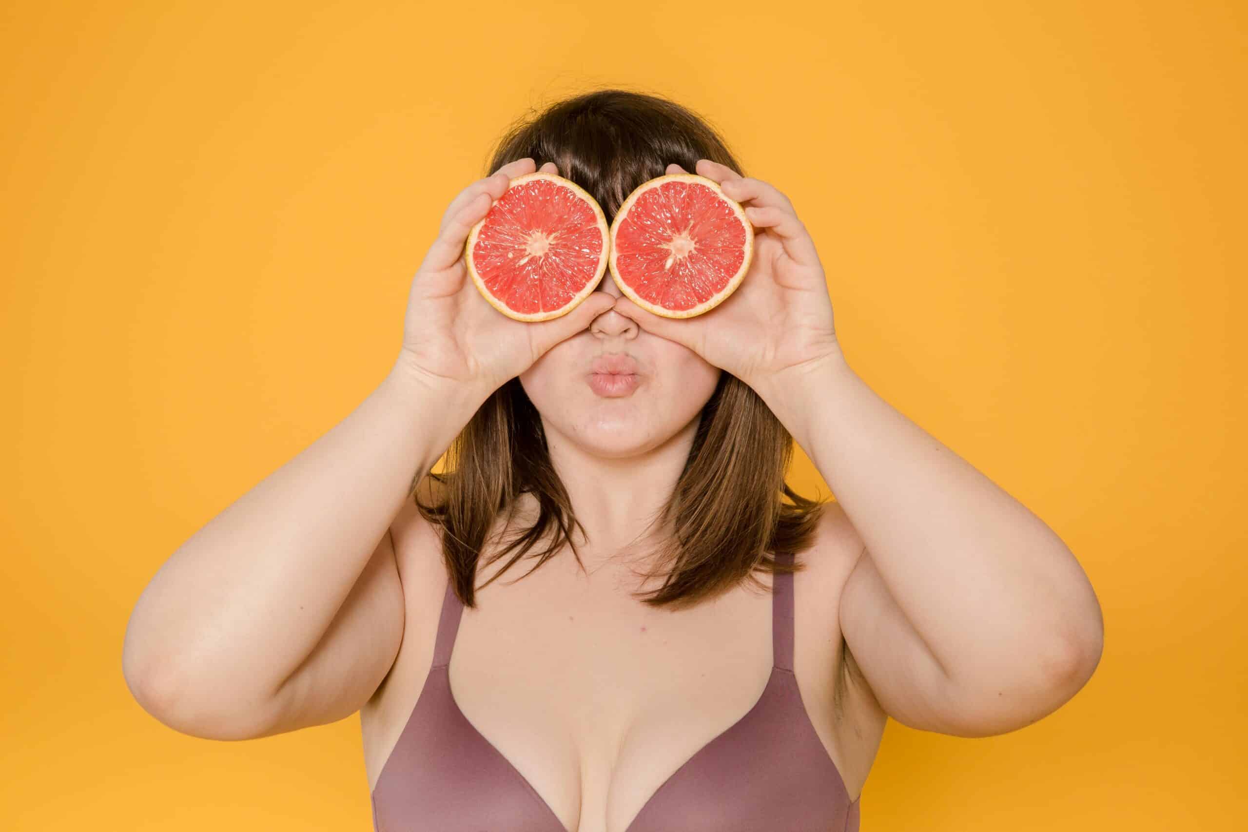 Eine mehrgewichtige Person im BH, die zwei Grapefruits vor ihren Augen hält